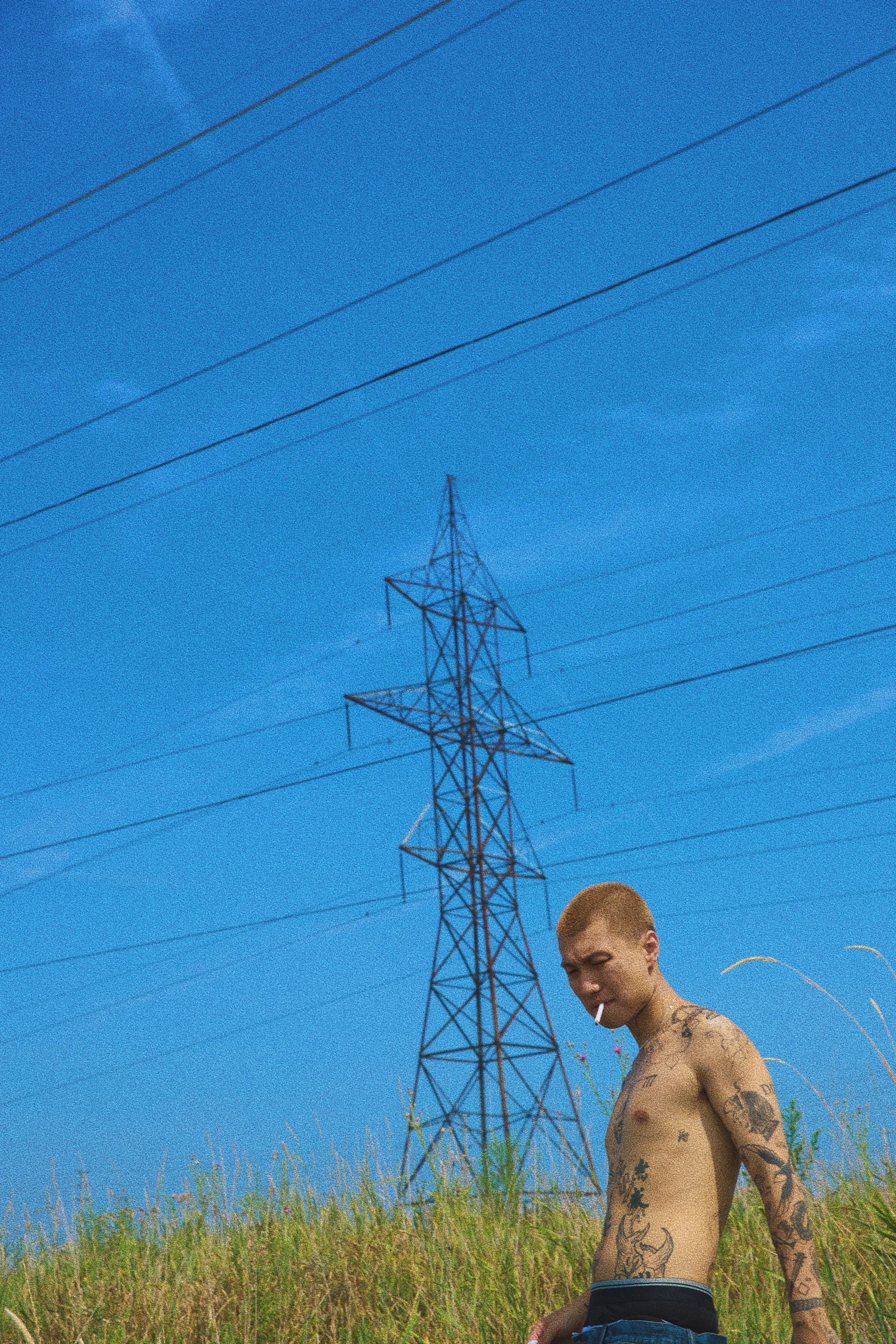 Yiwu Duan standing shirtless in tall grass under a transmission tower, Toronto